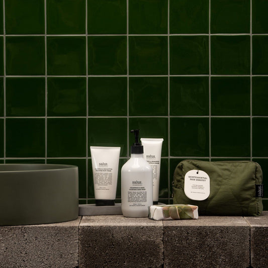 Bathroom setting with skincare products and a green pouch against a green tiled wall.